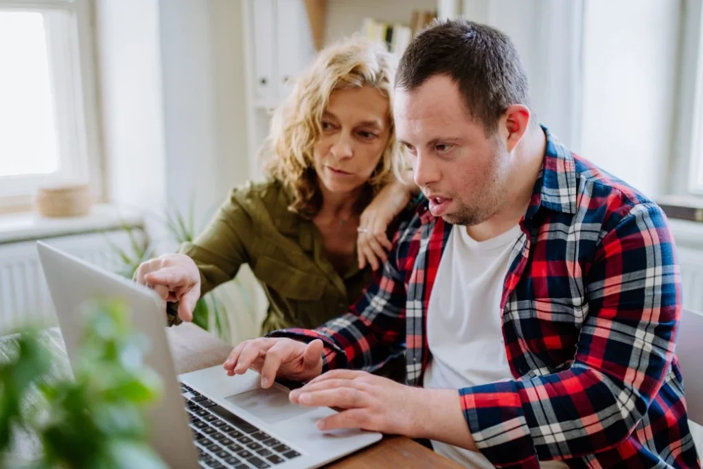 A disabled man with his support worker typing something in the laptop