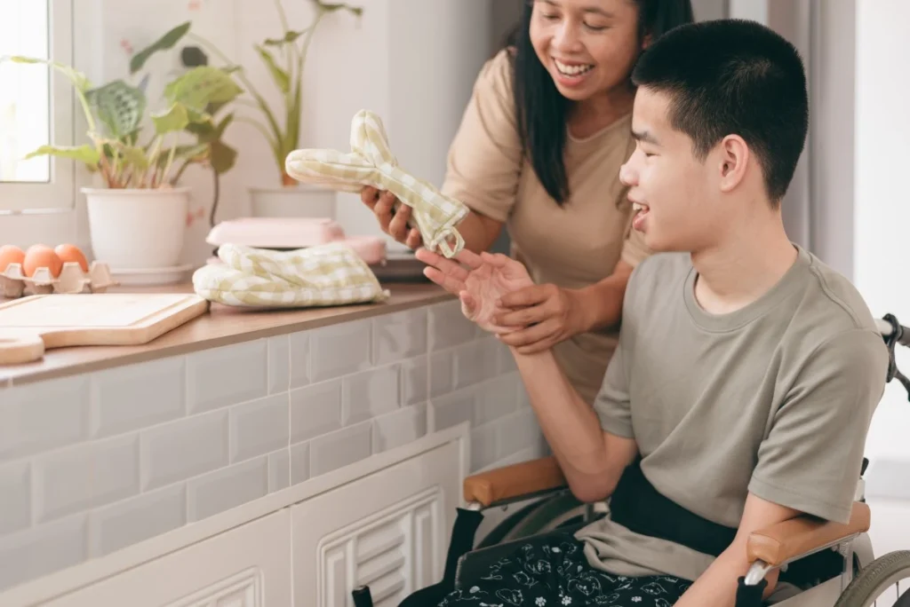 A disabled boy sitting in his wheelchair and his support worker in the kitchen