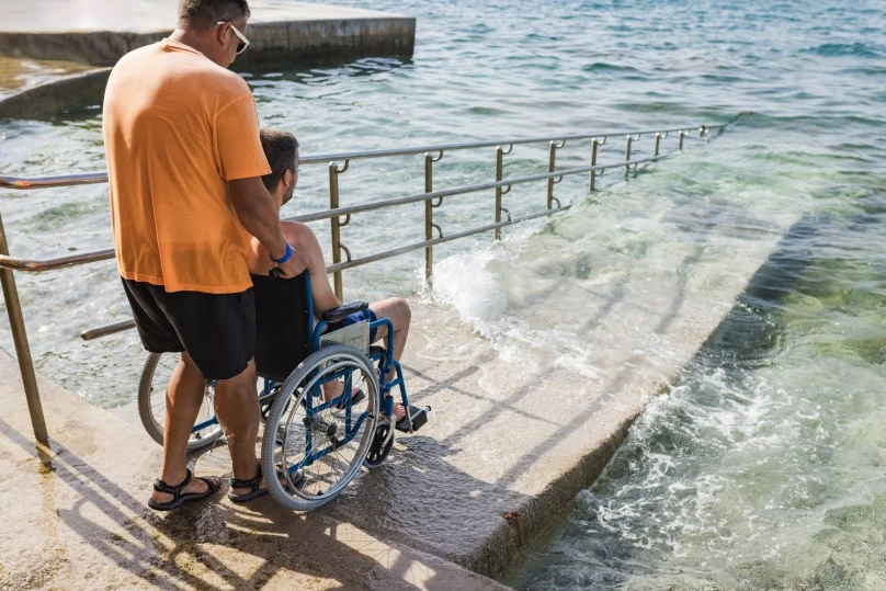 A disabled man in his wheelchair and his support worker on the beach