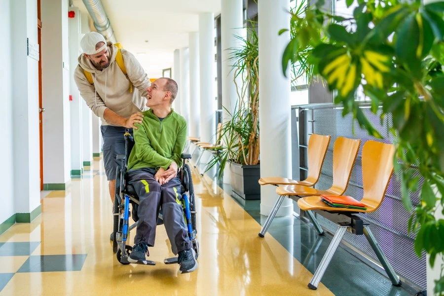 A disabled man sitting in his wheelchair smiling while looking at his support worker