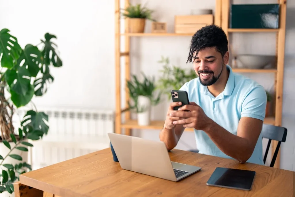 A man smiling while typing something on his phone