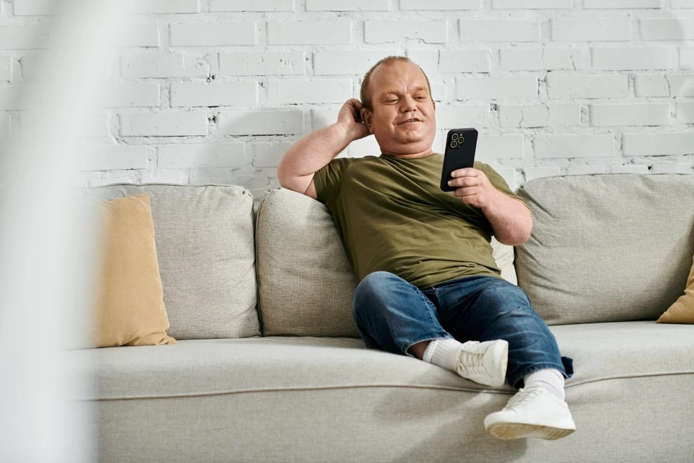 A man smiling while sitting down and looking at his phone